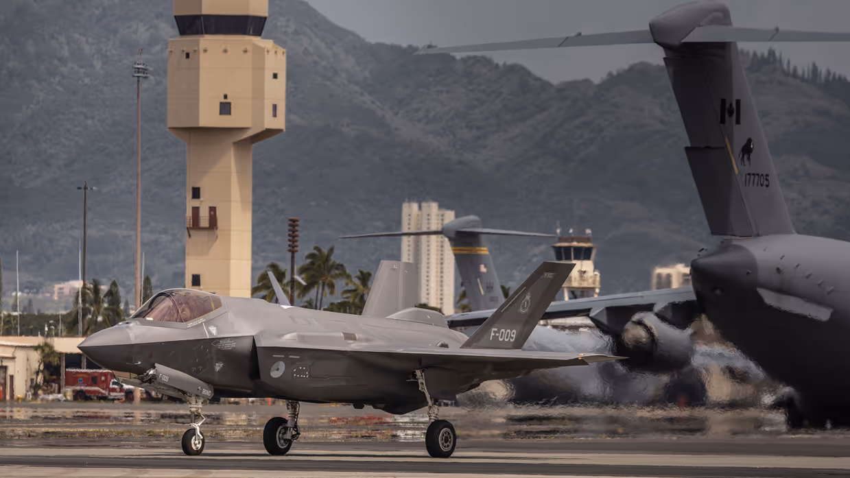 Een F-35 taxiet op Hawaii voor de verkeerstoren langs. In de achtergrond staan C-17 transportvliegtuigen van de VS en uit Canada