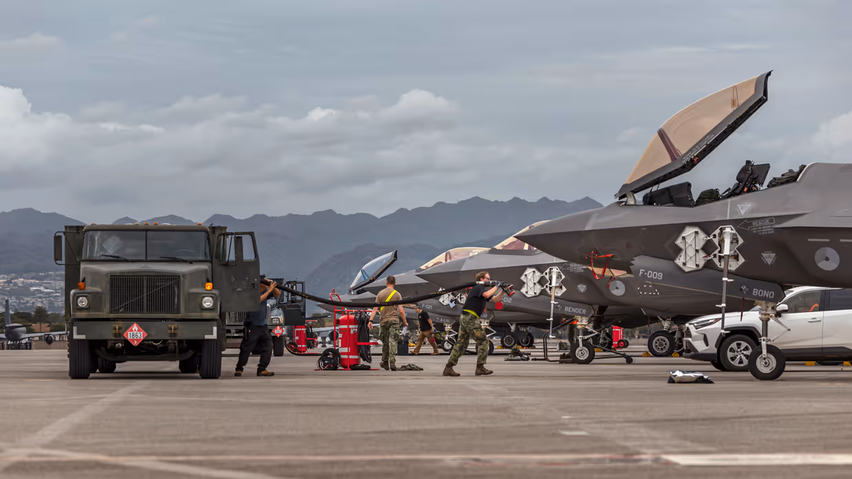 Luchtmachtpersoneel sjouwt brandstofslangen uit een Amerikaanse tankwagen naar een F-35. In de achtergrond zijn bergen te zien.