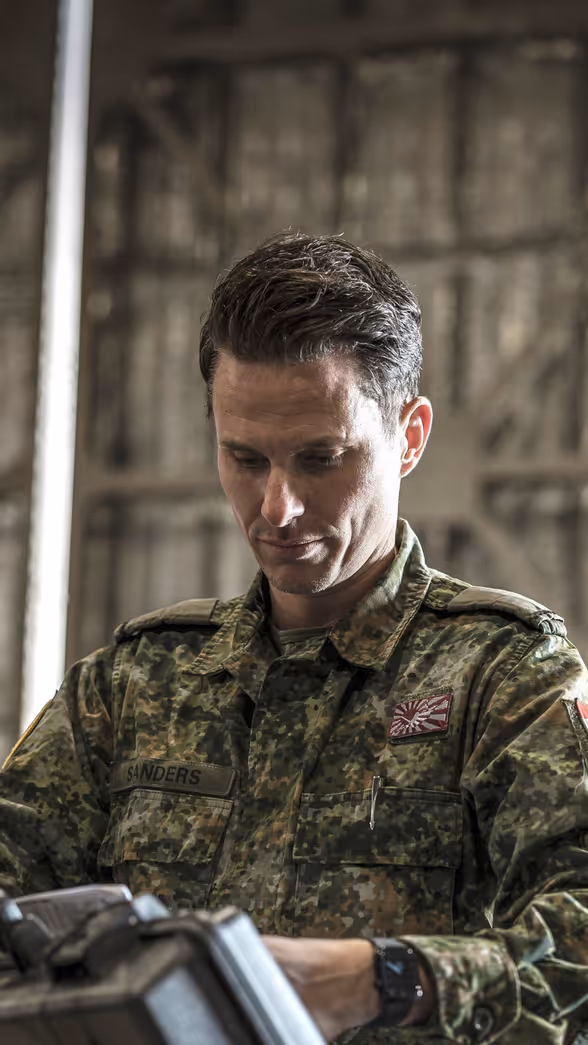 Een militair in een groen camouflagepak bekijkt een koffer die hij uit een container pakt.