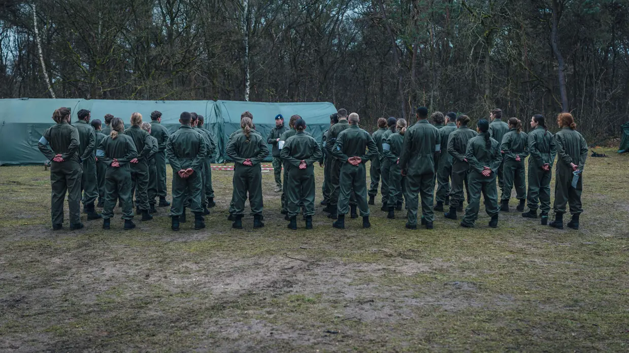 Militairen staan gegroepeerd in het bos voor een tent.