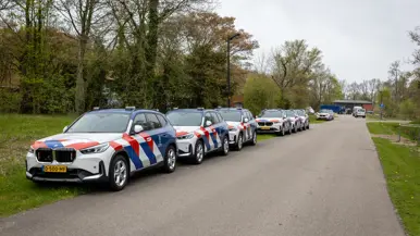 Voertuigen Marechaussee staan achter elkaar in de berm geparkeerd.
