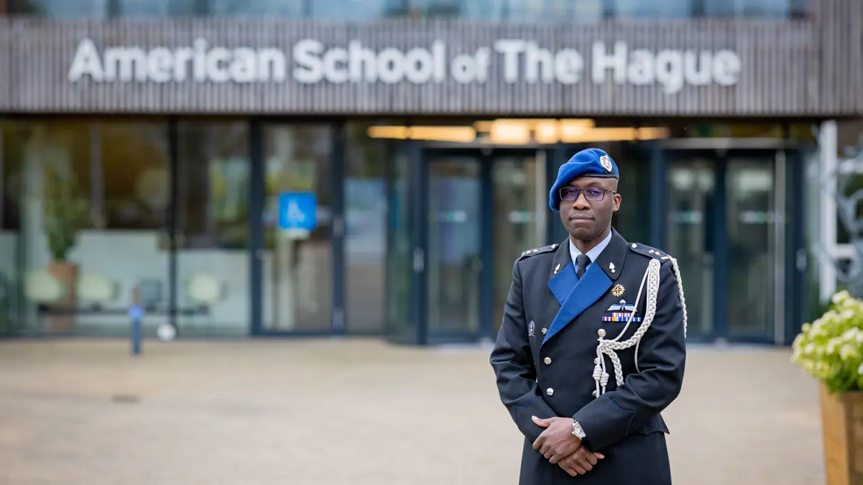 Marechaussee in uniform staat voor ingang schoolgebouw.