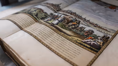 Een open, oud boek met een gekleurde tekening van een landschap, mensen, paarden en een kar, en geschreven tekst ernaast.