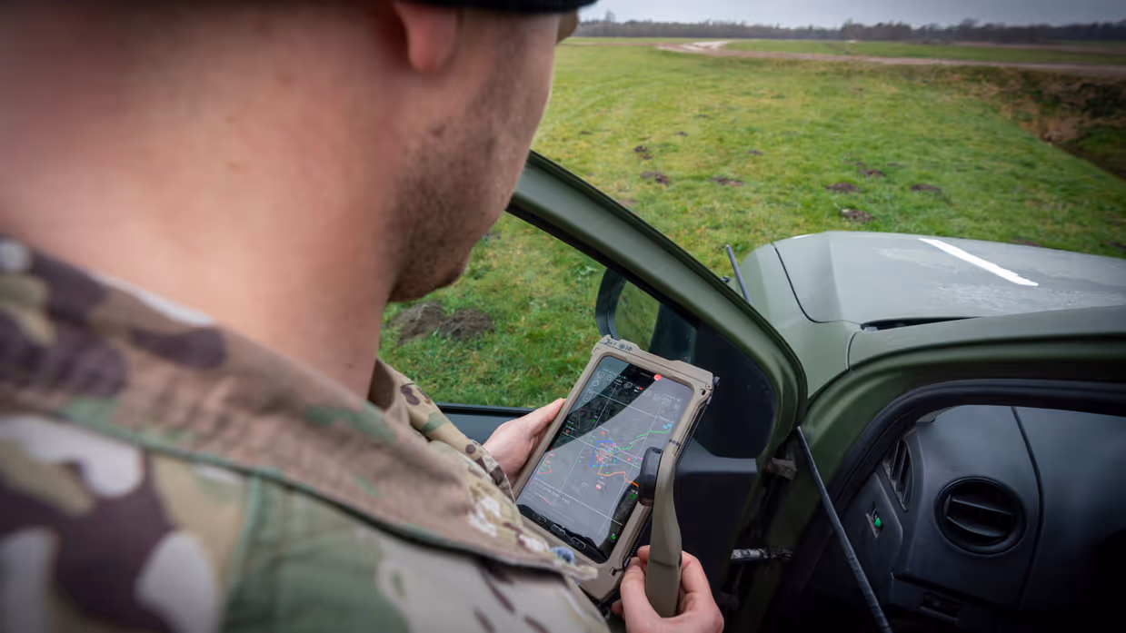 Over de schouder van een militair, naast zijn auto, zien we hem coördineren middels zijn smartphone.