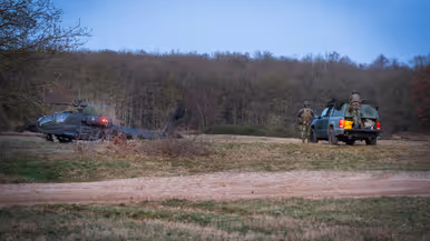 Een militaire helikopter staat stil in een veld, terwijl twee soldaten bij een groene terreinwagen met open laadbak staan. Rechts: het interieur van een helikopter tijdens zonsondergang. Twee piloten zitten in de cockpit, omlijst door oranje en donkere kleuren aan de lucht. 