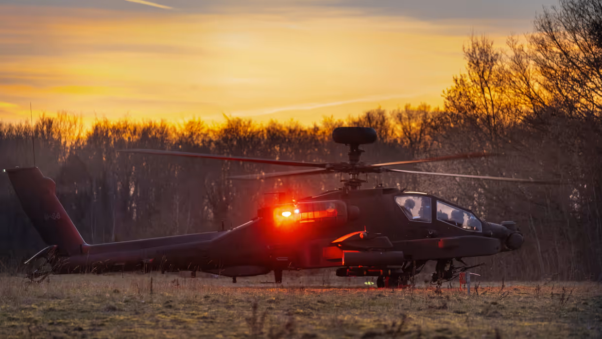Een Apache-helikopter staat aan de grond met een fel rode reflectie op het toestel van het schemerlicht.