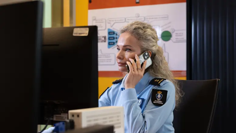 Luitenant-kolonel Irena zit achter een computer en houdt een telefoon bij haar oor.