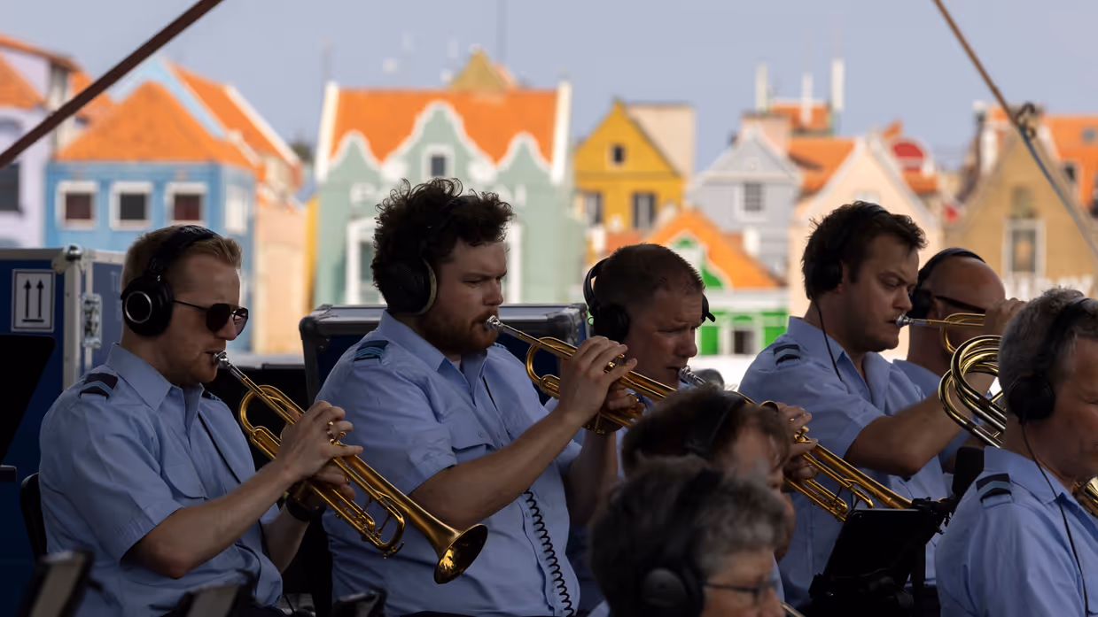 Orkestleden op blaasinstrumenten met op de achtergrond kleurrijke huizen. 