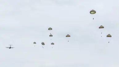 Parachutisten dalen met geopende parachutes neer boven de Belgische heide.