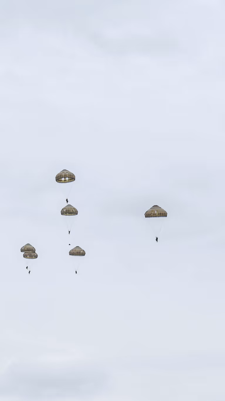 Parachutisten dalen met geopende parachutes neer boven de Belgische heide tijdens oefening Versatile Guard 