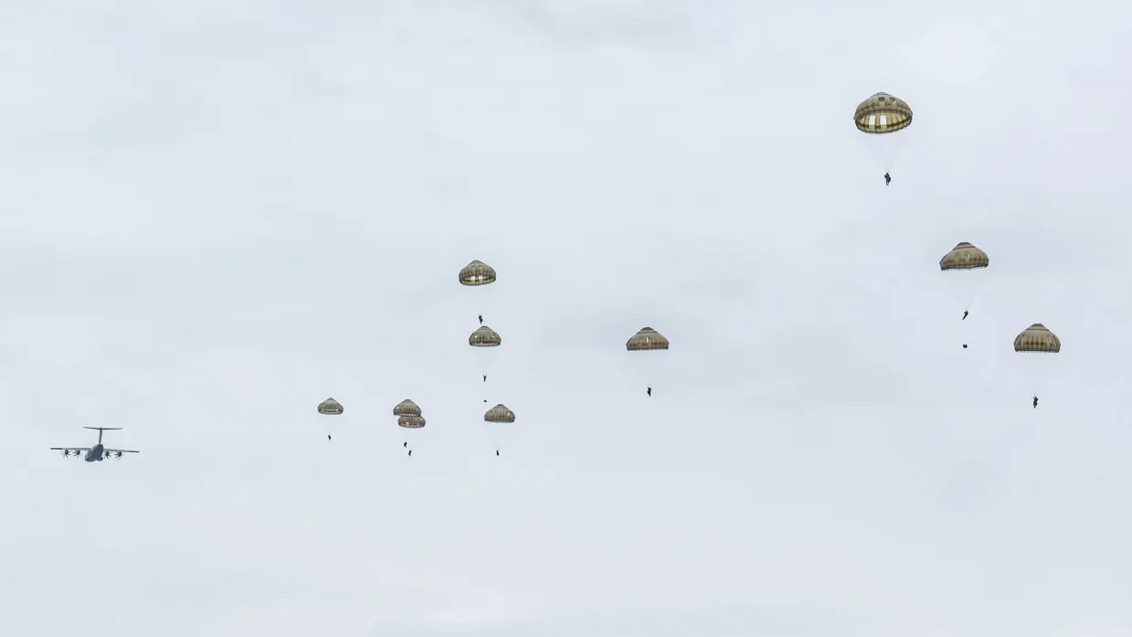 Parachutisten dalen met geopende parachutes neer boven de Belgische heide.