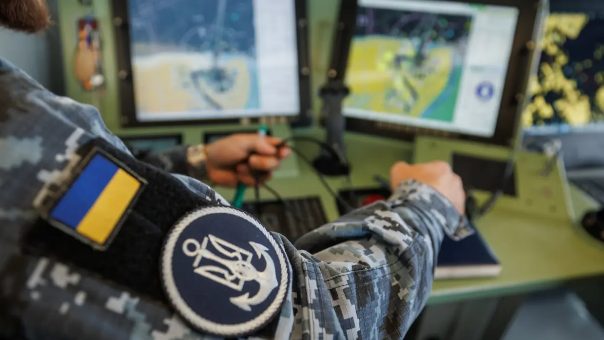Een militair op de brug, een militair kijkt aan dek door een verrekijker en een militair bedient apparatuur op de brug.