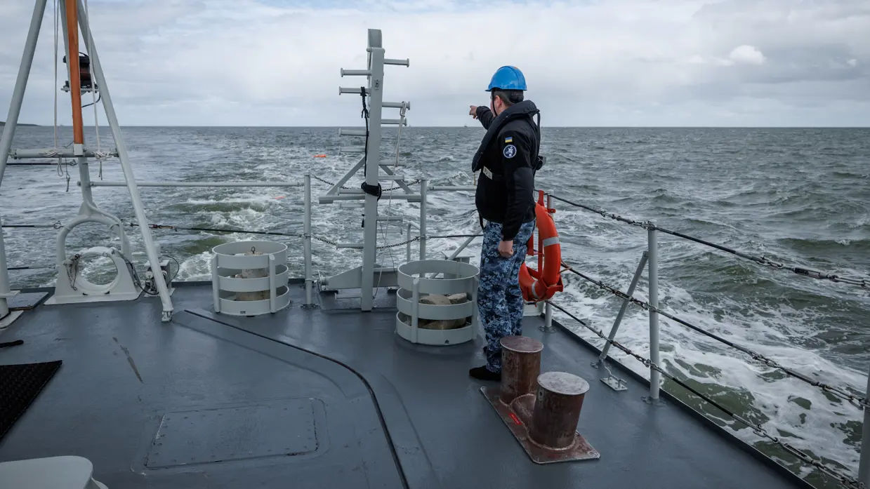 Een militair aan dek wijst naar iets in zee