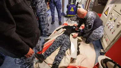 Militairen pakken tijdens de oefening de collega in die drenkeling speelt en warm moet worden gehouden en militairen behandelen deze oefengewonde in het schip.