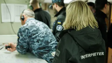 Een tolk met woord ‘interpreter’ op de rug staat achter een groepje militairen.
