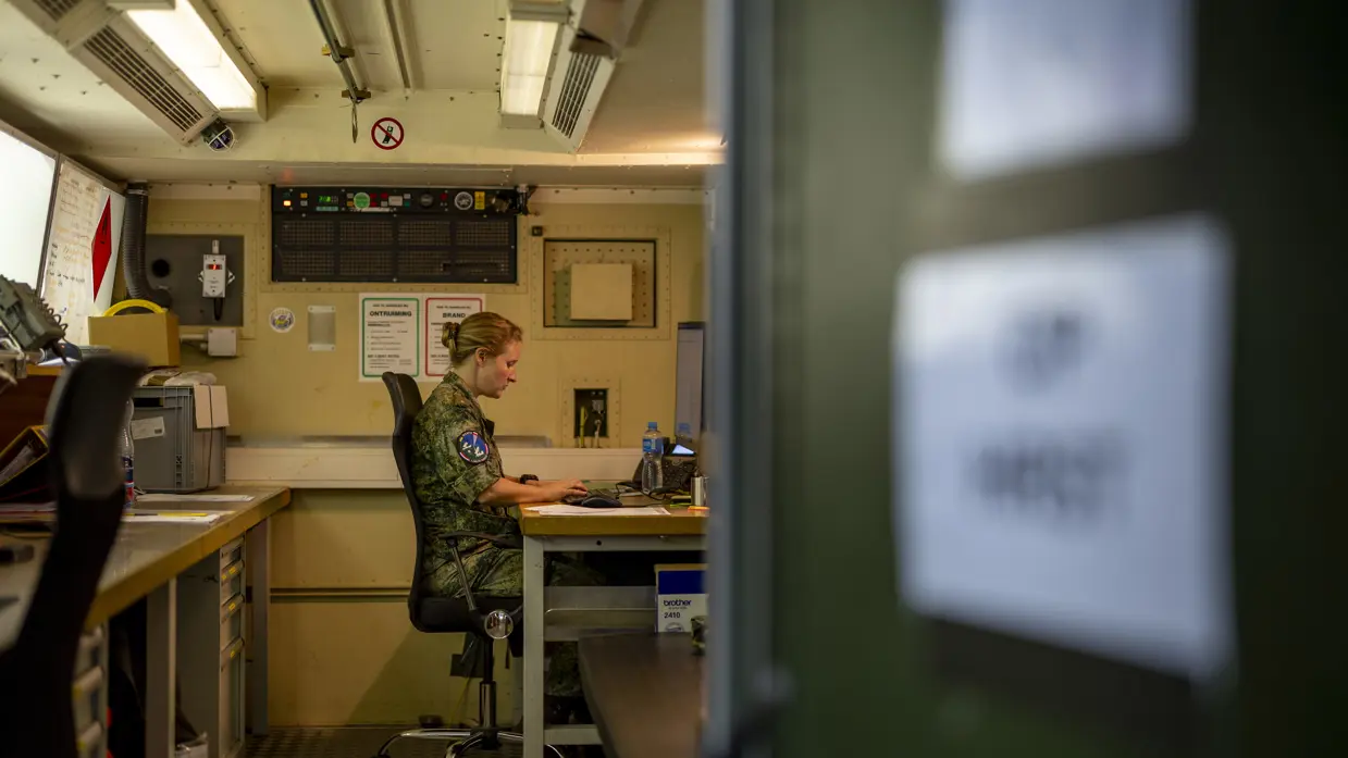 Op de linkerfoto zit Suzanne in haar werkcontainer achter de computer. Op de rechterfoto leunt Suzanne met een arm op een vrachtwagen.