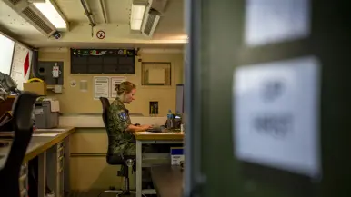 Op de linkerfoto zit Suzanne in haar werkcontainer achter de computer. Op de rechterfoto leunt Suzanne met een arm op een vrachtwagen.