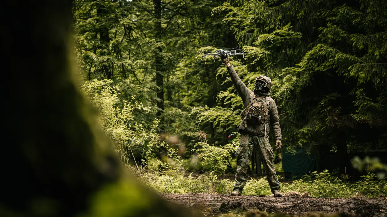 Een militair laat een drone opstijgen in het bos.
