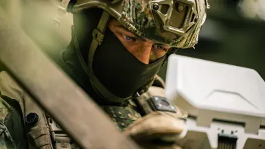 Een militair bestuurt een drone en kijkt geconcentreerd naar zijn afstandsbediening.
