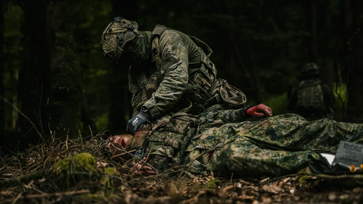 Bij een oefening helpt een militair een gewonde collega tijdens een ZHKH-casus. 