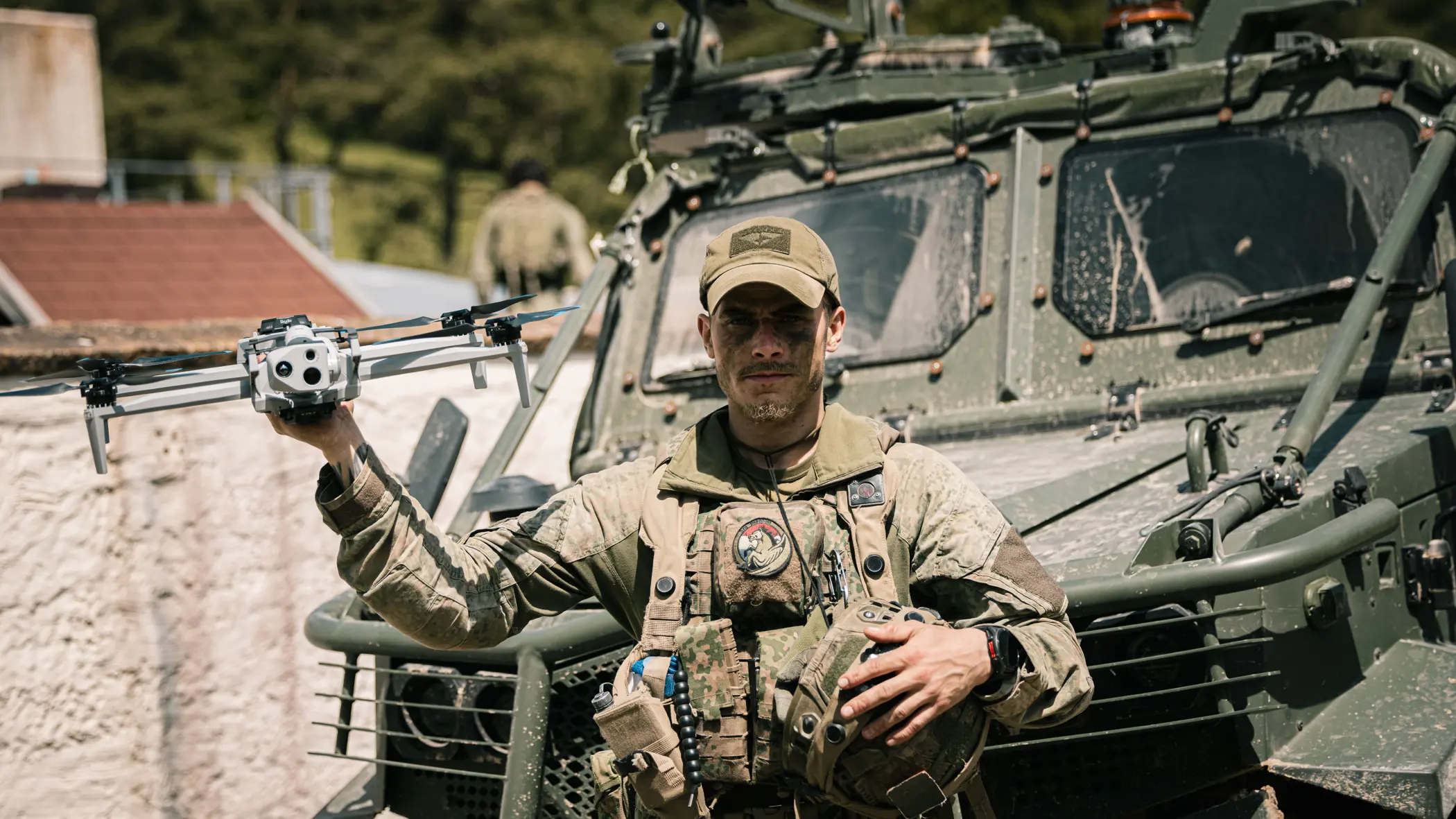 Een militair van de bevoorradingscompagnie van de Luchtmobiele Brigade voor een voertuig met een drone in zijn hand.