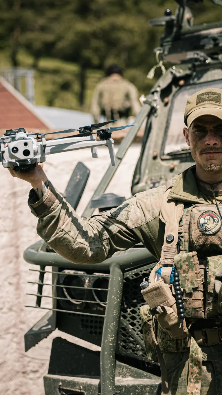 Een militair van de bevoorradingscompagnie van de Luchtmobiele Brigade voor een voertuig met een drone in zijn hand.