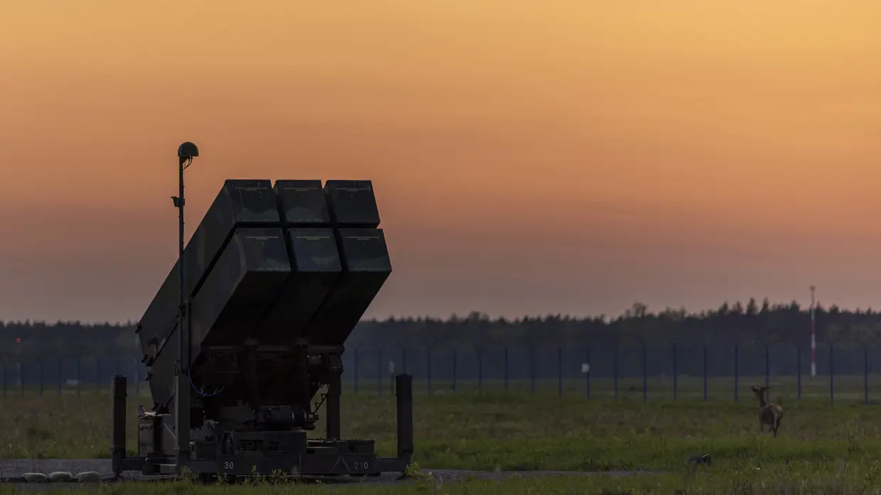 Op de linkerfoto een NASAMS-lanceerinrichting in het avondrood. Op de rechterfoto monteren militairen stabilisatievinnen op een luchtdoelraket.