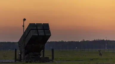 Op de linkerfoto een NASAMS-lanceerinrichting in het avondrood. Op de rechterfoto monteren militairen stabilisatievinnen op een luchtdoelraket.