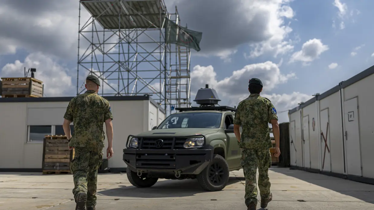 Op de linkerfoto lopen twee militairen naar een Amarok-legervoertuig met daarop een grijze bol. Op de rechterfoto zitten twee militairen in een Amarok-legervoertuig en kijken naar een scherm. 