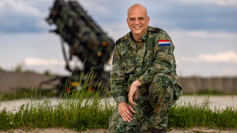 Maurice zit gehurkt op één knie. Op de achtergrond staat een Patriot-lanceerinrichting.