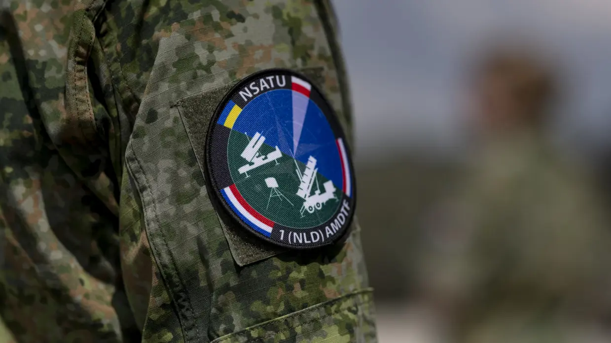 Mouwembleem van de AMDTF. Op het embleem zijn de diverse wapensystemen te zien plus de vlaggen van Nederland, Polen en Oekraïne.