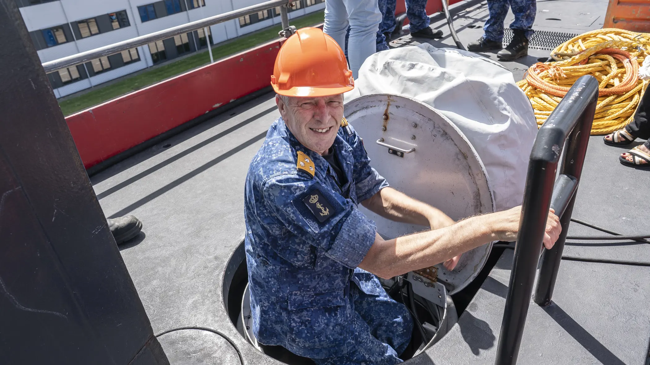 Een viceadmiraal met oranje bouwhelm klimt uit een onderzeeboot. 