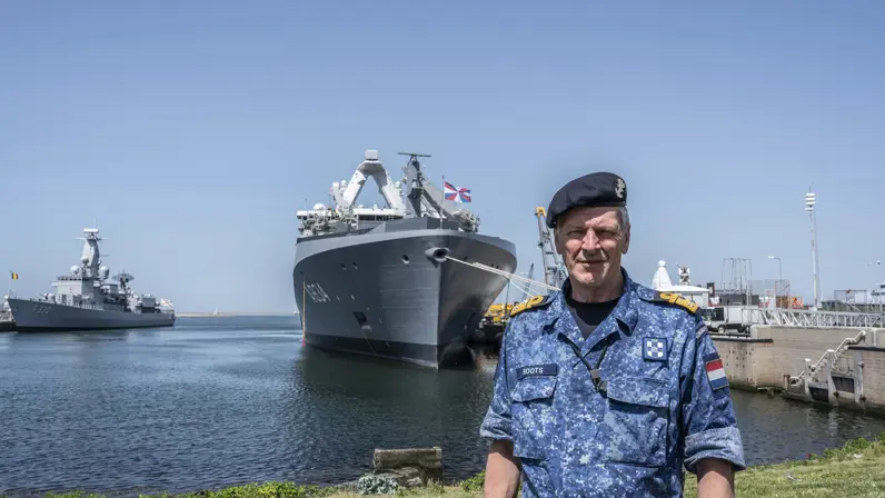 Vice-admiraal Boudewijn Boots poseert met baret op in de haven voor een marineschip. 