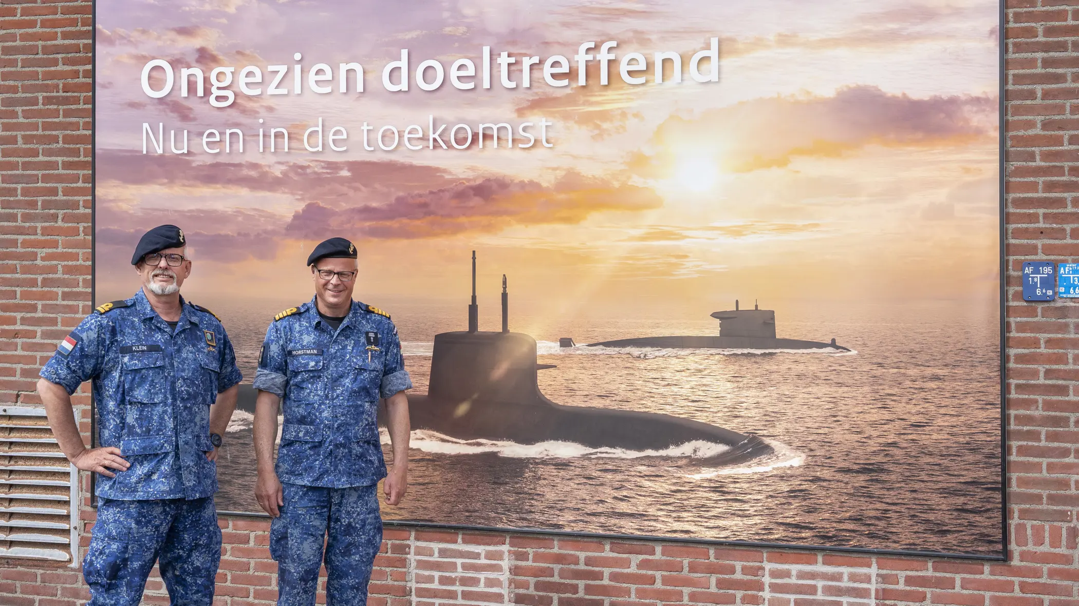 2 marinemannen poseren in uniform voor een billboard van de Onderzeedienst.