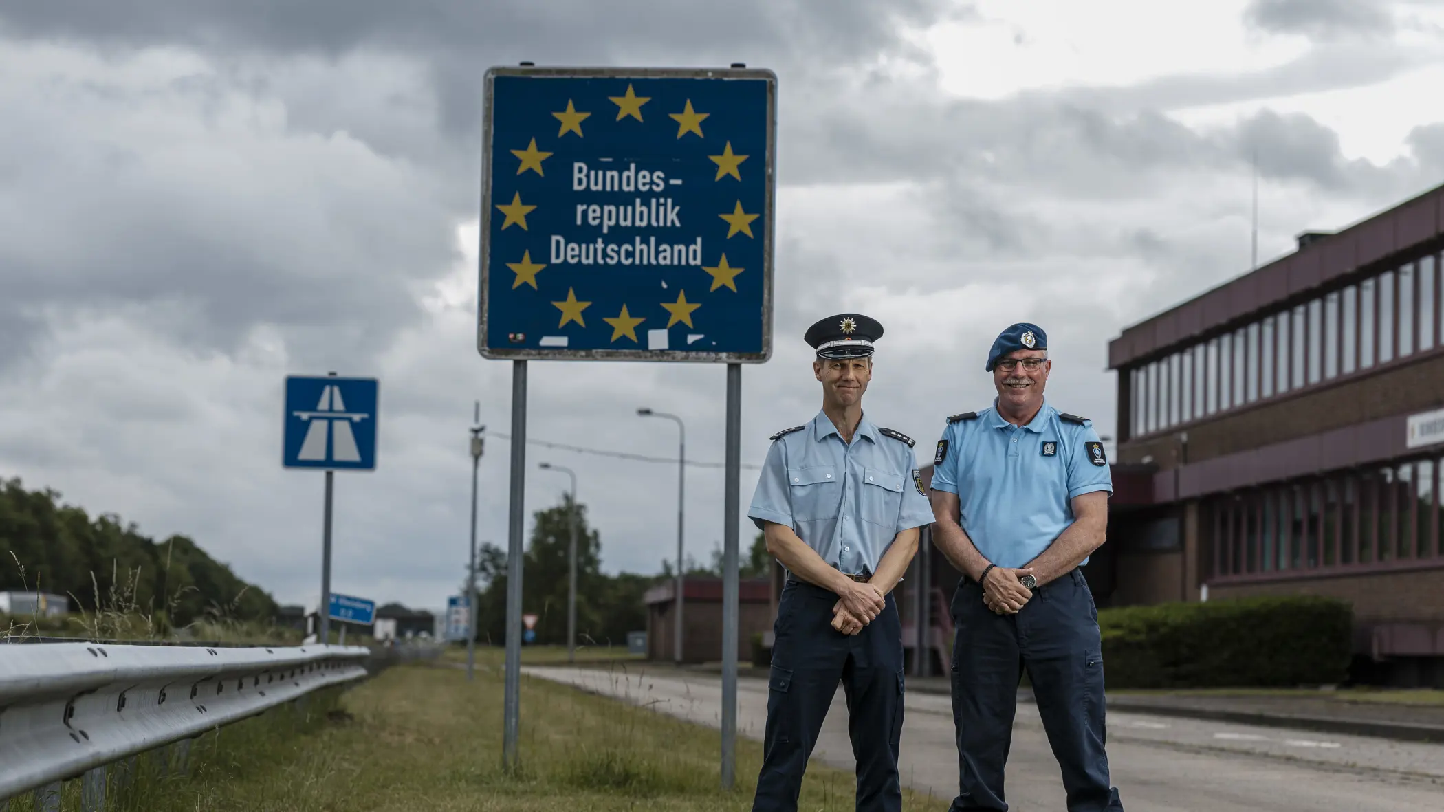 Eerste luitenant Herman en zijn Duitse evenknie voor een grensbord langs de snelweg. 