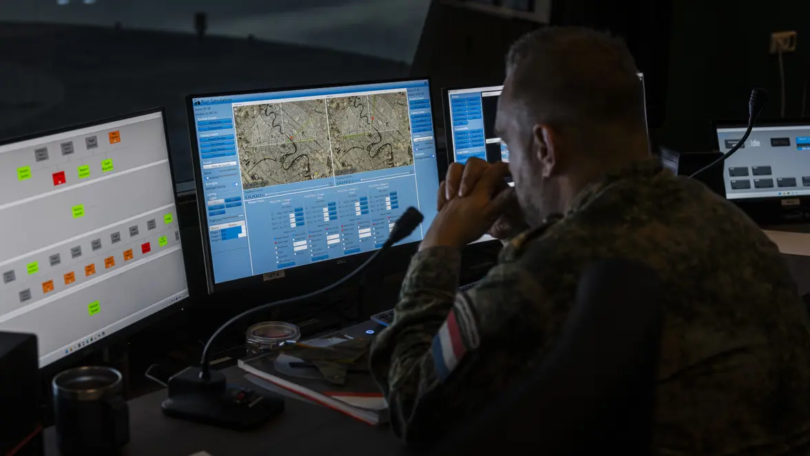 Een mannelijke militair in gevechtspak tuurt naar de schermen voor zijn neus.