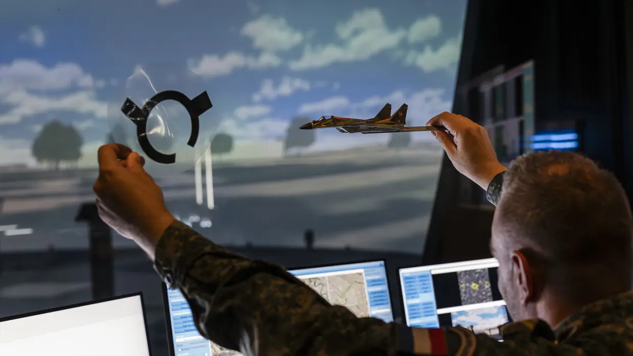 Een militair in de control room van de Stingerdome houdt een modelvliegtuig in de lucht.