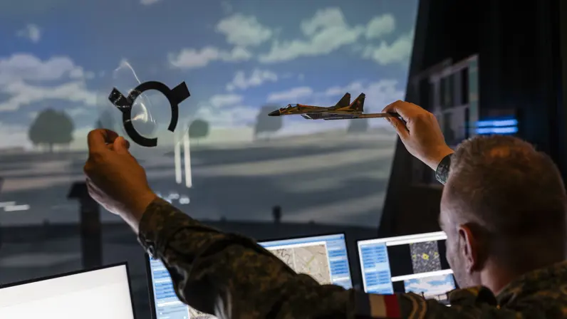 Een militair in de control room van de Stingerdome houdt een modelvliegtuig in de lucht.