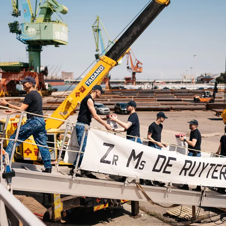 Bemanningsleden vormen een keten op de valreep en geven dozen aan elkaar door.