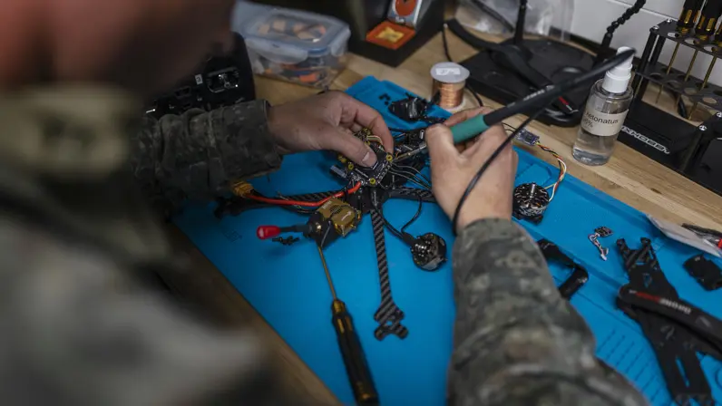 Een militair soldeert een drone op een werkbank in de mobiele werkplaats van TechDevOps tijdens oefening Fighter Lion.