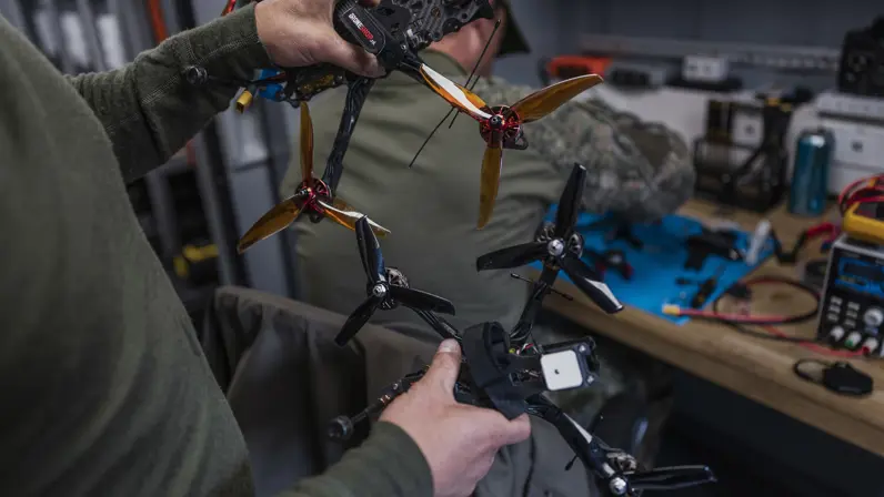 Militairen vergelijken twee drones in de mobiele werkplaats van TechDevOps tijdens oefening Fighter Lion.