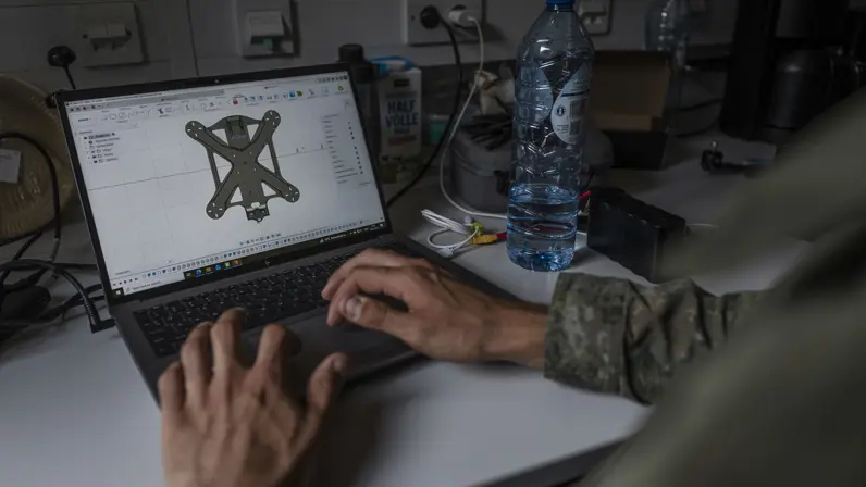 Een militair ontwerpt een nieuw onderdeel voor een drone op een laptop in de mobiele werkplaats van TechDevOps.