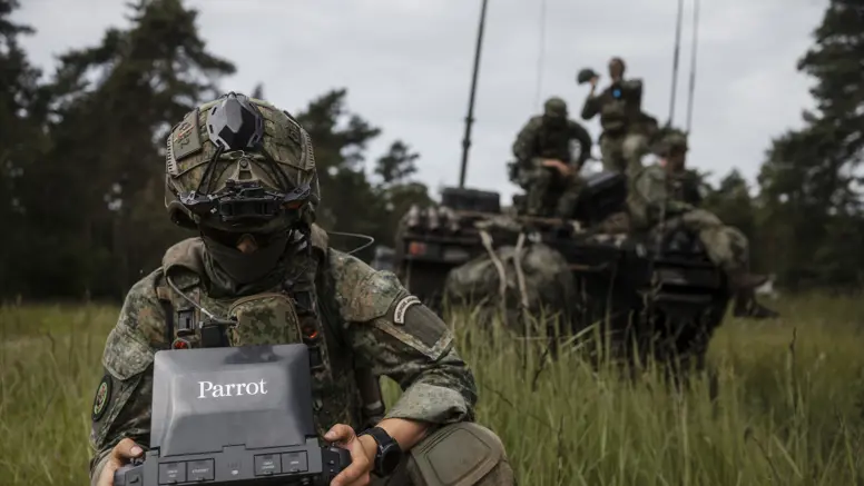 Een militair bereidt een dronevlucht voor tijdens oefening Fighter Lion, terwijl collega's op de achtergrond de operatie coördineren.