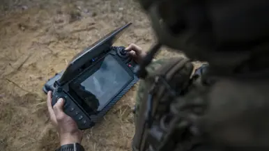 Een militair bedient tijdens oefening Fighter Lion de grondcontroller van een drone en bekijkt de livebeelden op het scherm.