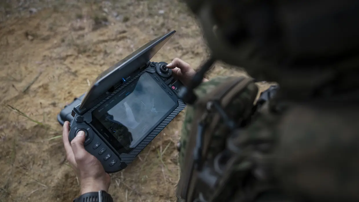 Een militair bedient tijdens oefening Fighter Lion de grondcontroller van een drone en bekijkt de livebeelden op het scherm.