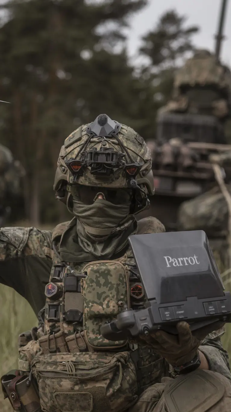 Een militair tijdens oefening Fighter Lion houdt een Parrot-verkenningsdrone omhoog terwijl hij de controller vasthoudt.
