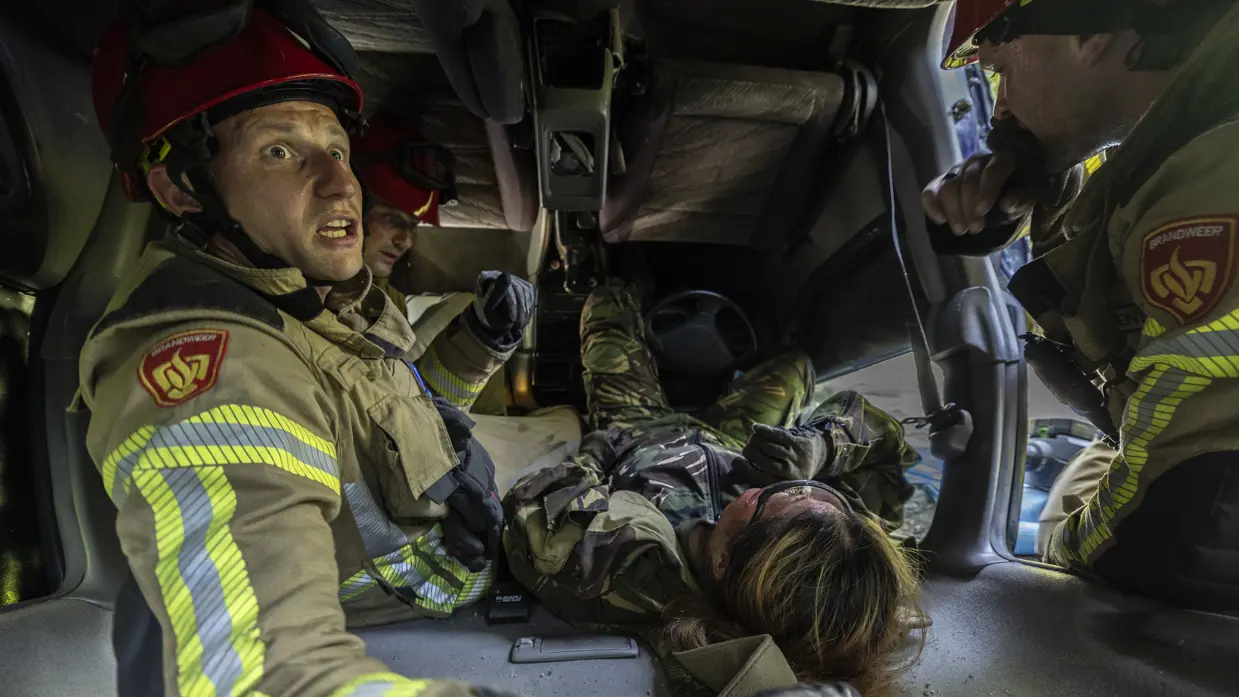 De brandweer probeert een bekneld iemand onder een auto te bevrijden.