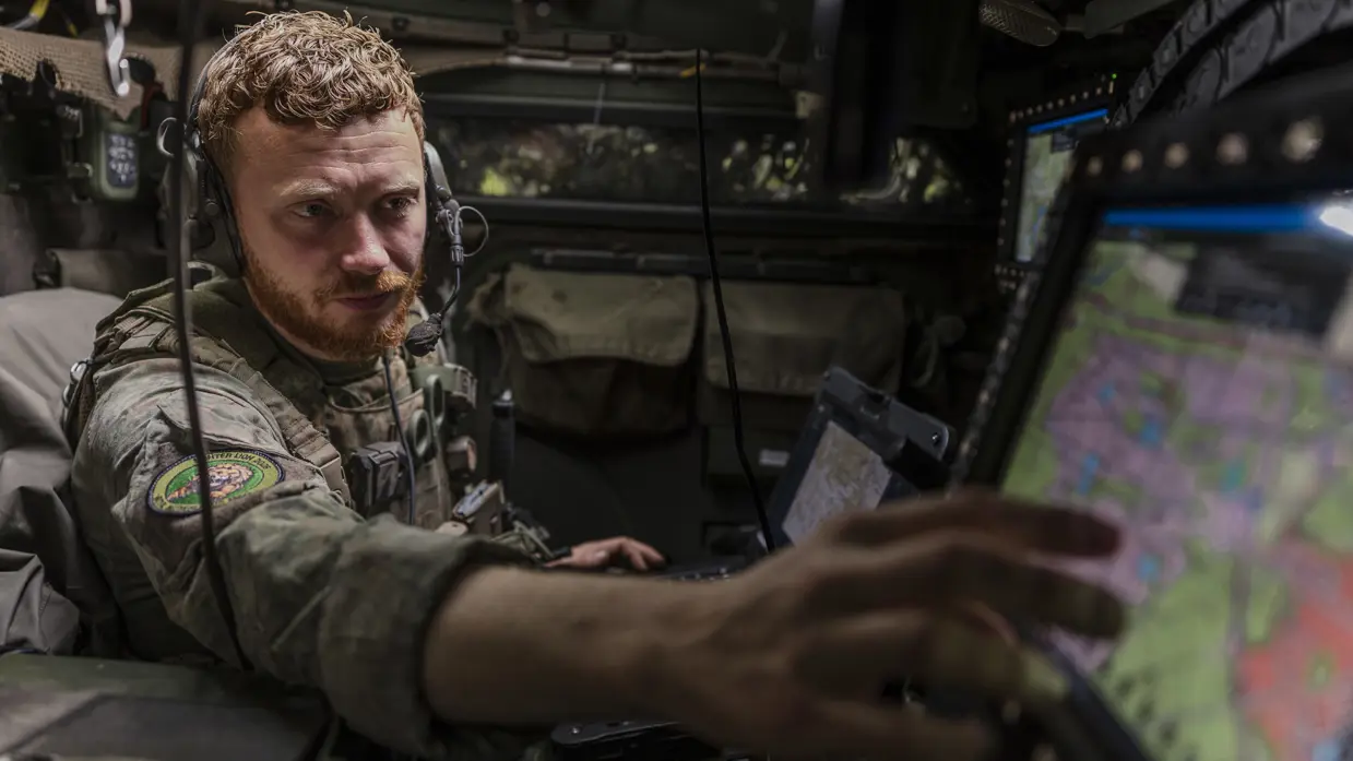 Een Forward Observer werkt in een commandovoertuig achter digitale schermen en beoordeelt meldingen van het AITAS-systeem.