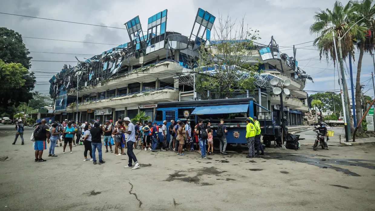 Een rij Venezolanen staat bij een hulppost, op de achtergrond een ingestort gebouw.