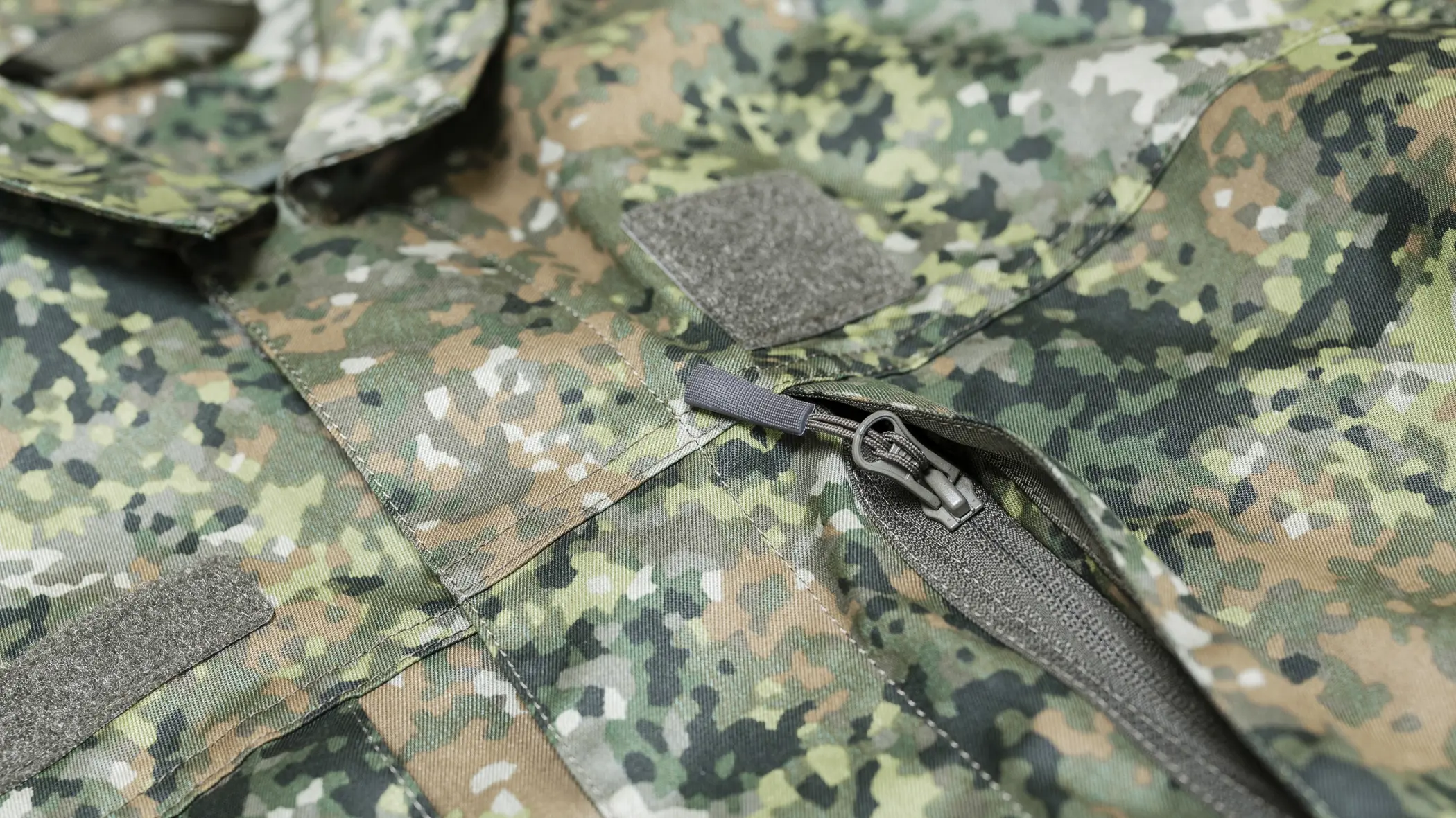 Detail van rits borstzak op militair pak in groen camouflagepatroon.
